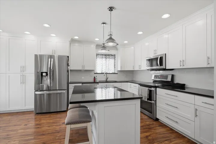 White shaker cabinetry with dark countertops, stainless steel appliances, and wood-finish flooring