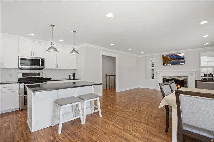 Kitchen island with pendant lighting, stainless steel appliances, wood-finish flooring, white cabinetry, and a fireplace with a white mantel
