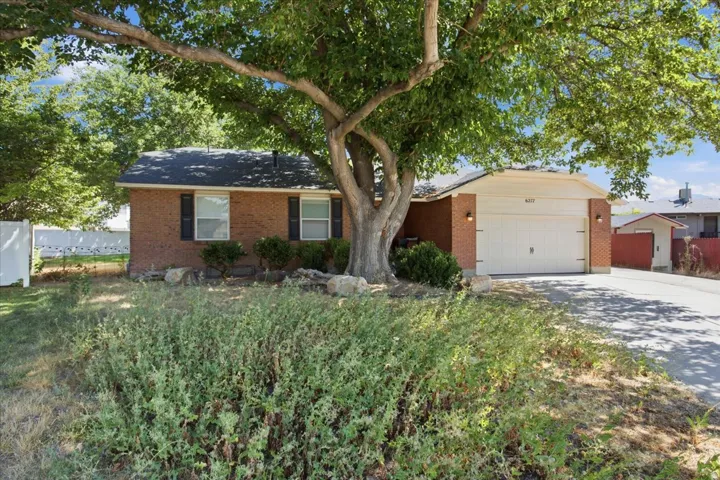 Brick exterior with a prominent mature tree, attached two-car garage, and a paved driveway