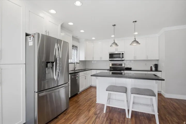 Kitchen featuring white shaker cabinetry, stainless steel appliances, dark countertops, a central island, and wood-finish flooring