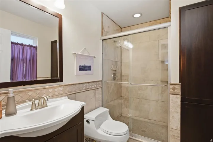 Tile-surround shower with a glass enclosure, wood-finish vanity with an integrated sink, and an embedded wall cabinet