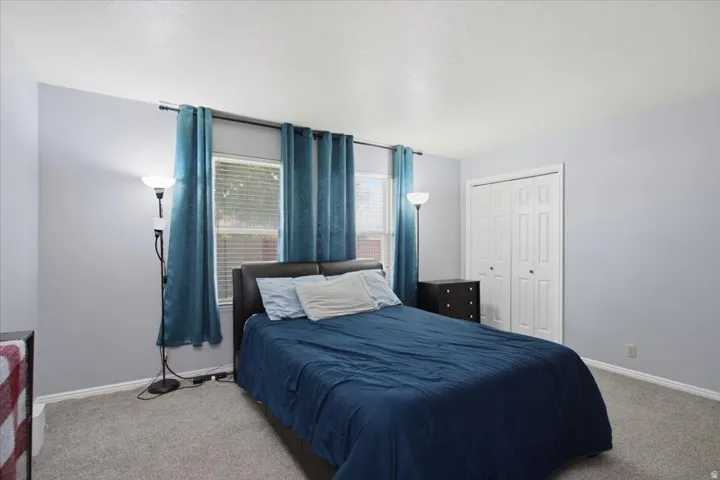 Light gray wall paint, textured ceiling, two windows with blinds, bi-fold closet doors, and gray carpet flooring