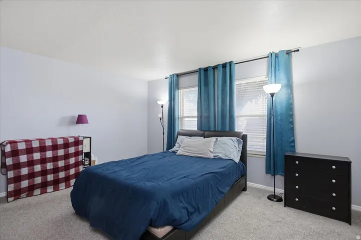 Plush carpet flooring complements light wall tones in this spacious room featuring two windows with horizontal blinds