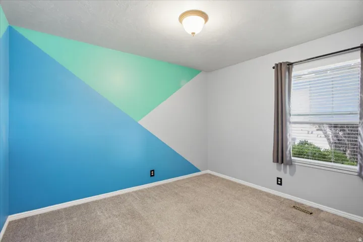 Carpeted room with a geometric accent wall and a single window with blinds