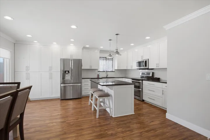 Kitchen featuring wood-finish flooring, white cabinetry, dark countertops, a central island with pendant lighting, and stainless steel appliances