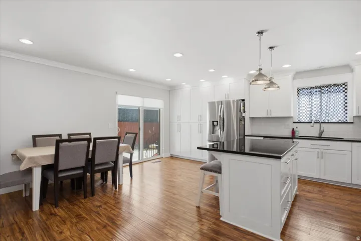 Open-concept kitchen featuring wood-finish flooring, white cabinetry, dark countertops, and a kitchen island with pendant lighting
