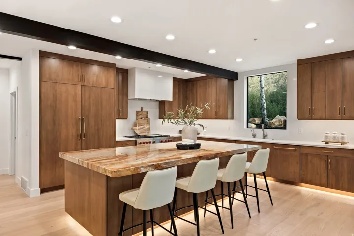 Gourmet kitchen with custom wood cabinetry, a large center island featuring a unique stone countertop, integrated appliances, and light wood-finish flooring