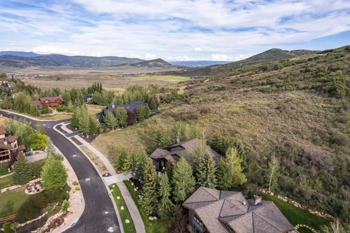 Paved residential street with curving design, landscaped properties, mature trees, and mountainous terrain