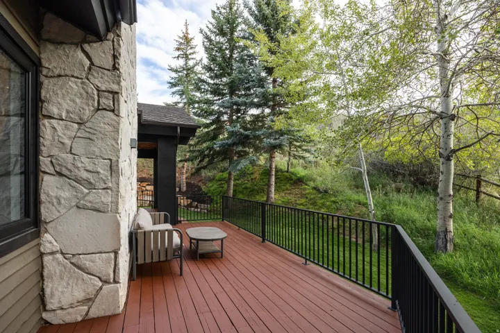 Expansive outdoor deck with rich wood-finish flooring, featuring a dark metal railing and stone exterior accents
