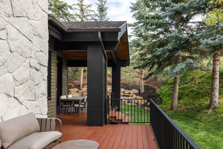 Exterior stone cladding, wood decking, dark-painted structural columns, and black metal railings with mature trees