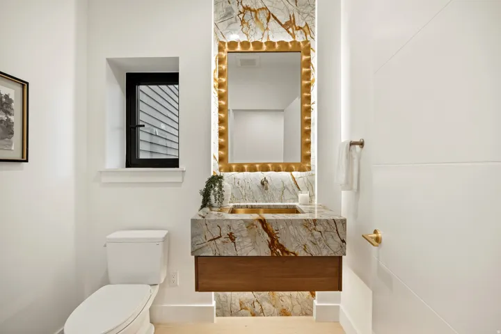 Floating wood-finish vanity with a vessel sink and stone countertop, complemented by a lighted mirror and stone accent wall