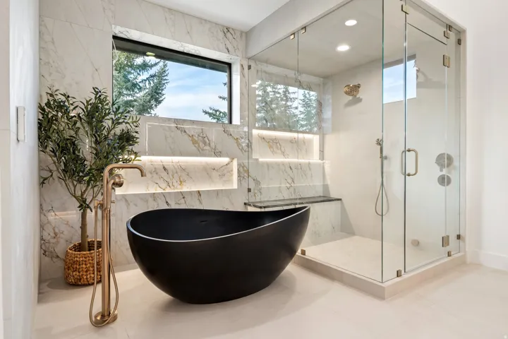 Freestanding soaking tub with floor-mounted fixture, walk-in shower with glass enclosure, wall-mounted marble-finish tile, and a built-in shower bench