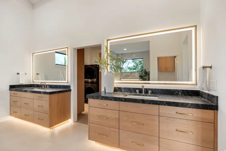 Dual wood-finish vanities with stone countertops, undermount sinks, and integrated lighting