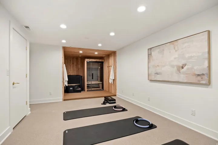 Recessed lighting illuminates the carpeted room, featuring a built-in sauna with wood paneling and a dedicated platform