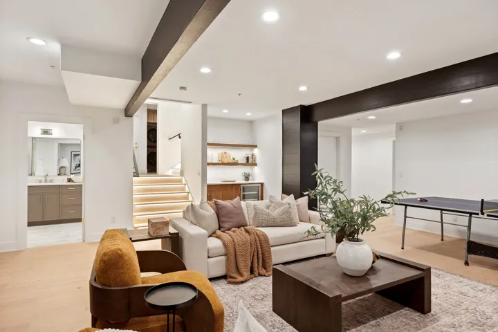 Spacious recreation area featuring light wood-finish flooring, recessed lighting, and a built-in wet bar with open shelving