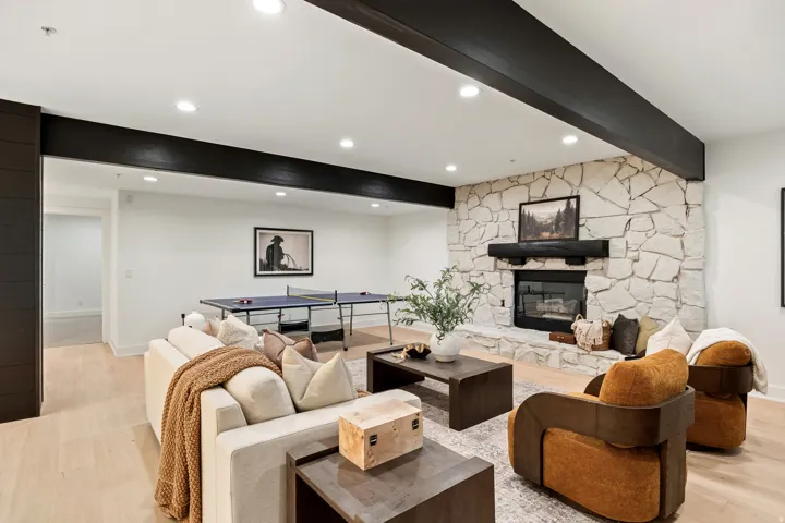 Spacious recreation room featuring a stone-clad fireplace, wood-finish flooring, recessed lighting, and exposed ceiling beams