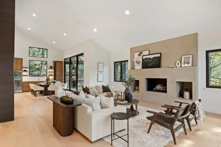 Vaulted ceiling with recessed lighting, integrated fireplace with built-in niches, light wood-finish flooring, and black-framed windows