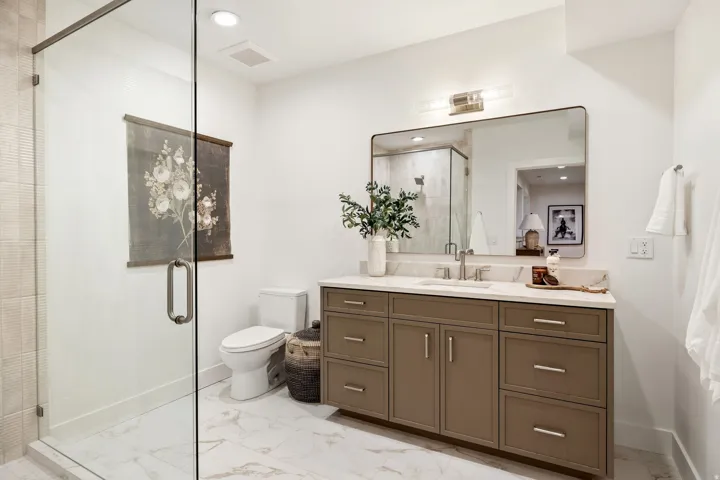 Frameless glass shower enclosure, single vanity with ample storage, integrated sink, and undermount lighting