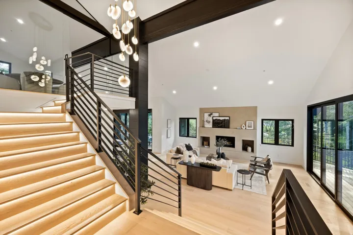 Vaulted ceilings, a built-in fireplace feature wall with integrated shelving, expansive glass panel doors, and a wood-finish staircase with embedded lighting