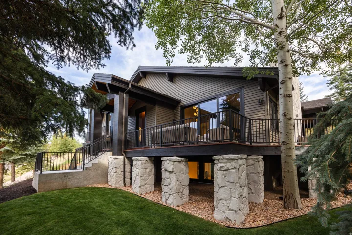 Multi-level exterior with dark siding, expansive decking, and stone pillar supports