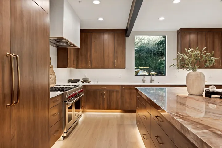 Spacious kitchen featuring rich wood cabinetry, integrated stainless steel appliances, a large center island with a stone countertop, under-cabinet lighting, and light wood-finish flooring