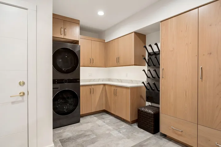 Integrated laundry appliances, light wood-finish cabinetry, white countertops, a tiled flooring, and a built-in storage system