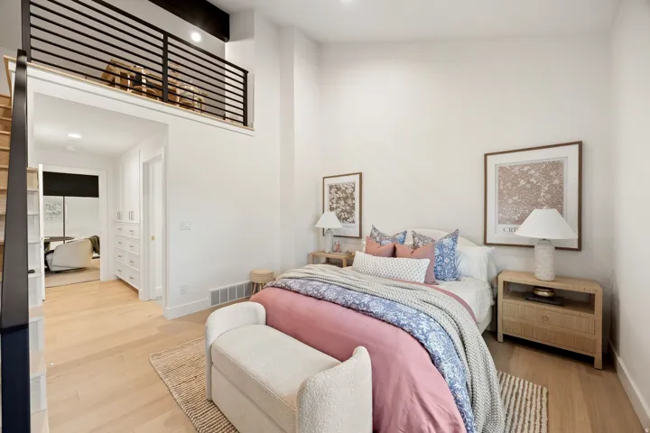 High ceilings with exposed wood beams, light wood-finish flooring, built-in storage cabinetry, and a loft with horizontal metal railings