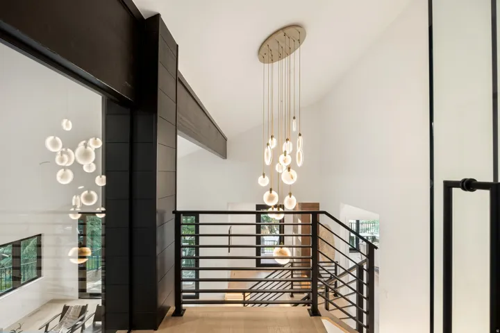 Vaulted ceiling with an elongated chandelier, black metal railings, wood-finish flooring, and structural black beams