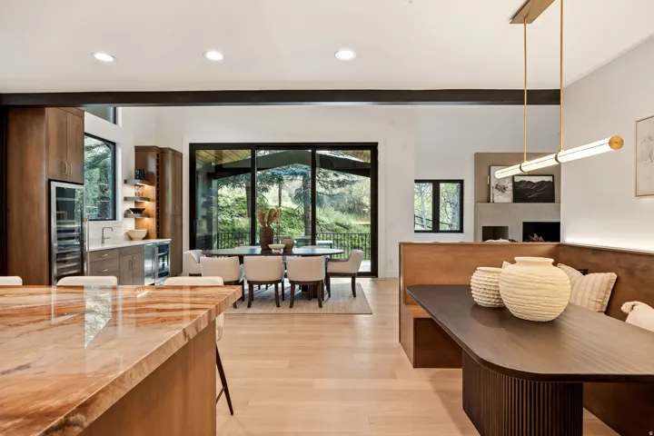Wood-finish flooring throughout, integrated kitchen cabinetry, built-in beverage refrigerator, sliding glass doors to outdoor area, and a built-in dining nook