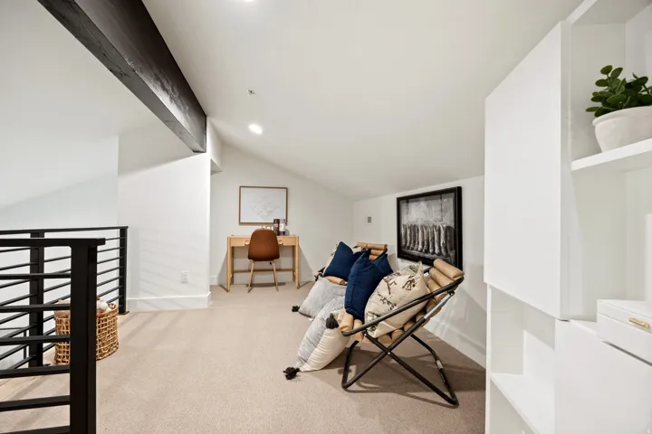 Vaulted ceiling with exposed beam, recessed lighting, built-in shelving, carpeted flooring, and metal railing