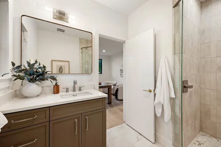 Transitional bathroom featuring a single vanity with a white countertop and undermount sink, a large rectangular mirror, a three-light vanity fixture, and a glass-enclosed shower with tiled walls