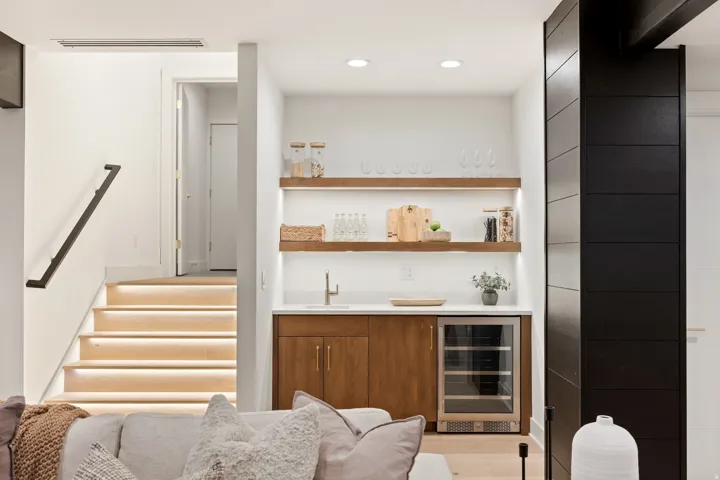 Custom wet bar with wood-finish cabinetry, integrated beverage refrigerator, and open shelving with integrated lighting