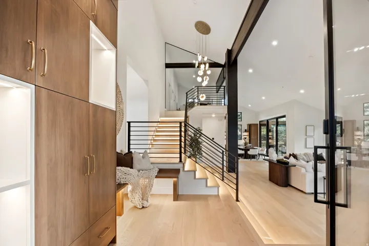Open-concept entry with wood-finish flooring, built-in cabinetry with illuminated display niches, and a grand staircase featuring metal railings and illuminated treads