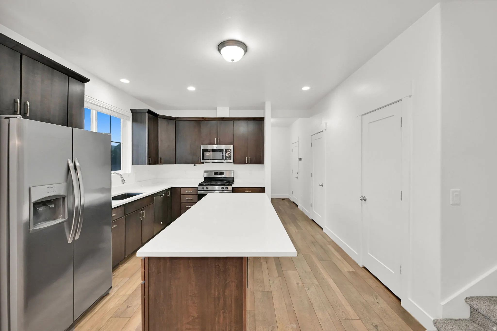 Kitchen featuring dark wood cabinetry, stainless steel appliances, a white solid surface island, and wood-finish flooring