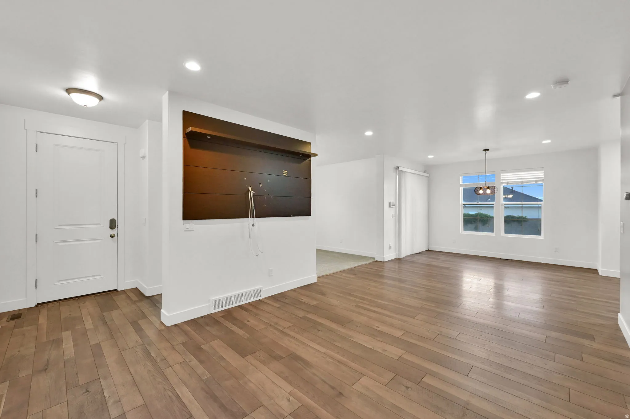 Expansive open-concept living space featuring wood-finish flooring throughout, a modern built-in entertainment niche, recessed lighting, and a contemporary chandelier