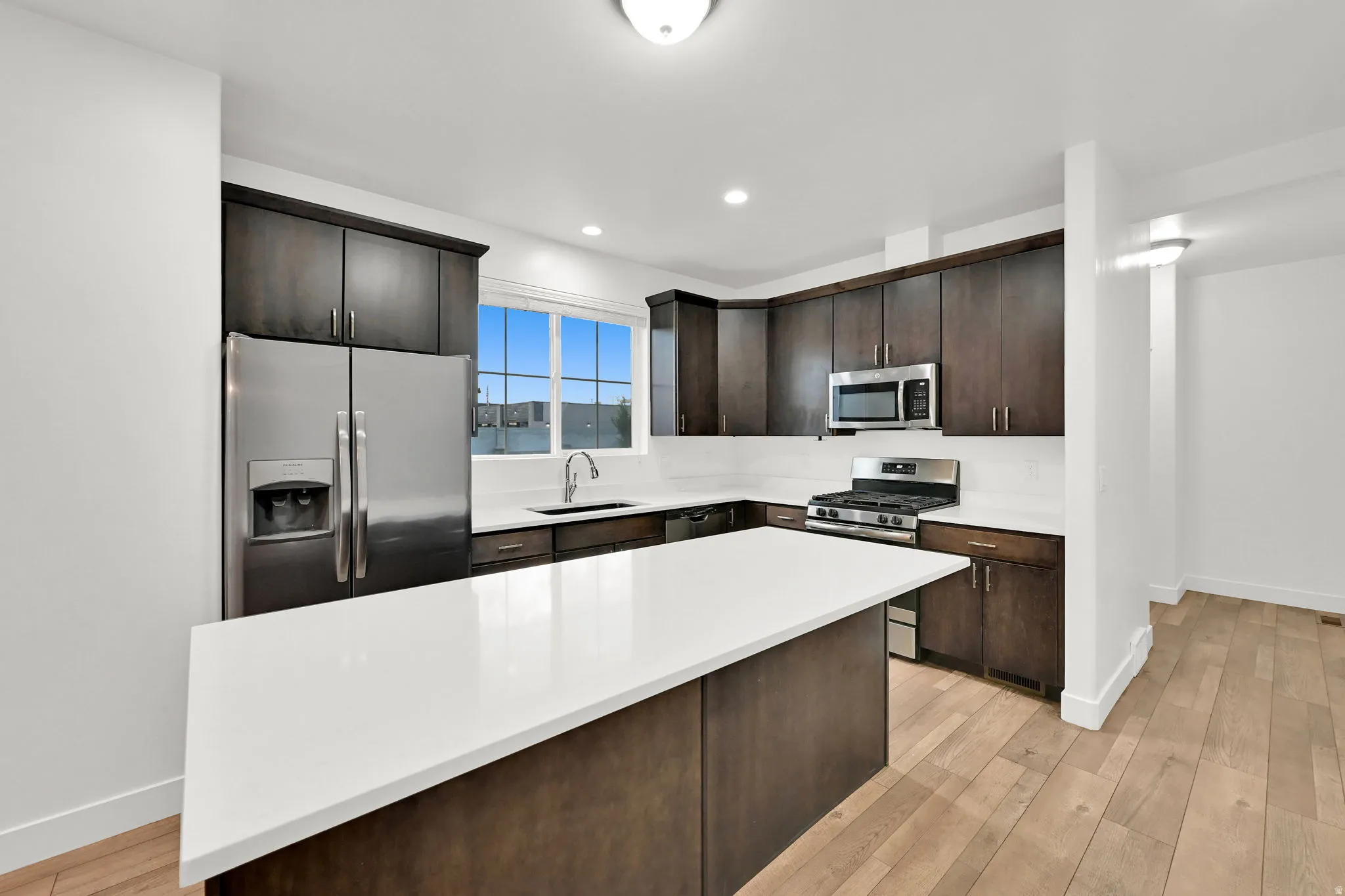 Open-concept kitchen with dark wood-finish cabinetry, white countertops, stainless steel appliances, and a central island