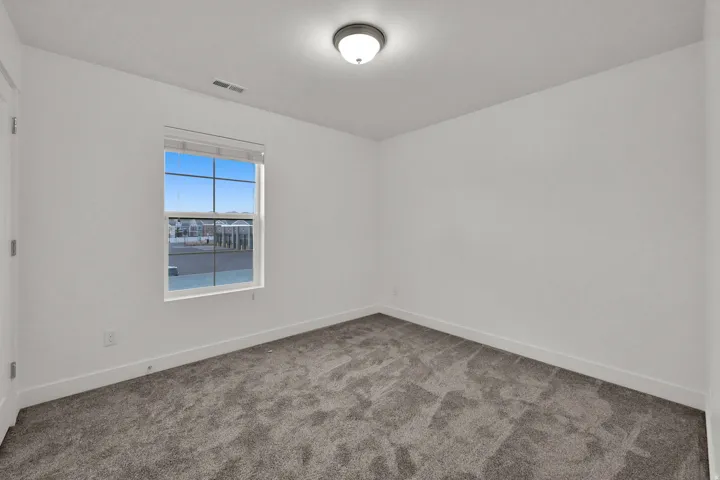Neutral tone wall finishes, grey textured carpeting, and a window with a roller shade