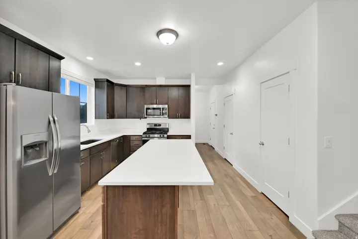 Kitchen featuring dark wood cabinetry, stainless steel appliances, a white solid surface island, and wood-finish flooring