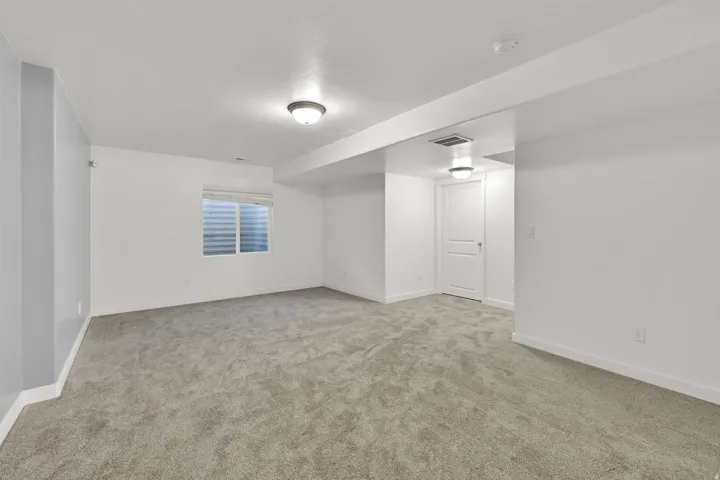 Spacious room with plush gray carpeting, white walls, and a window with blinds