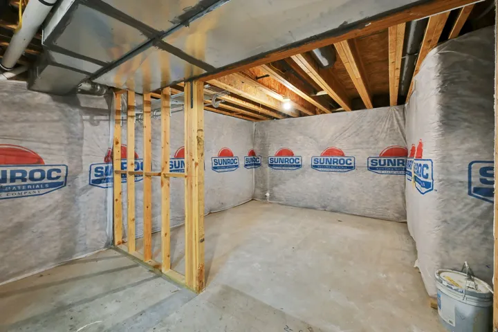 Unfinished basement space featuring exposed wood framing, concrete flooring, and insulated walls