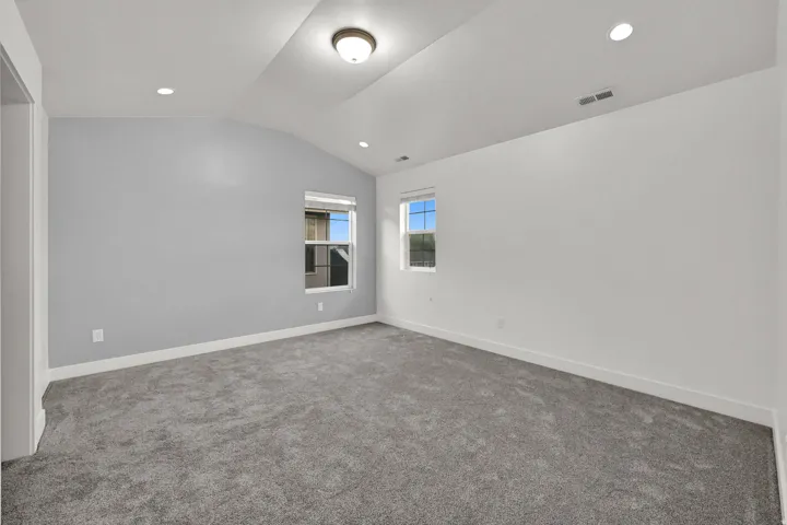 Vaulted ceilings with recessed lighting, gray carpeting, a two-tone wall finish, and two windows
