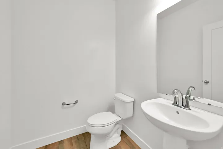 Pedestal sink with chrome faucet, wall-mounted mirror, and wood-finish flooring