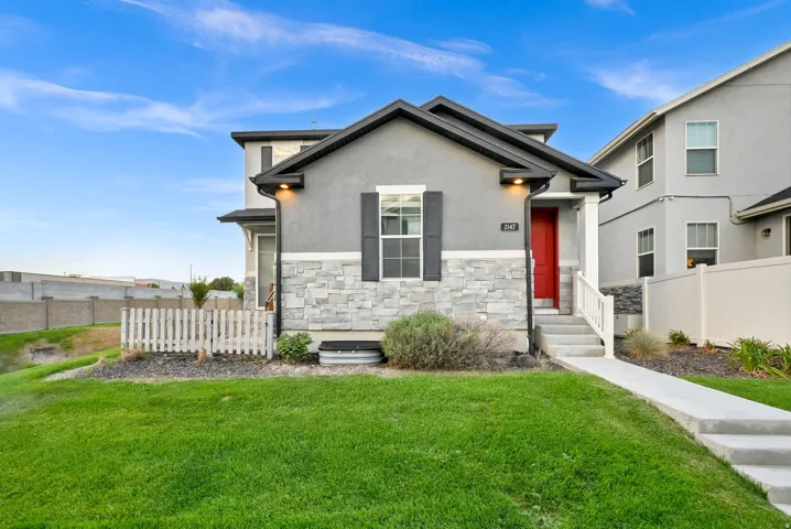 Stucco exterior with stone accent siding, contrasting dark shutters, a vibrant red entry door, and a concrete walkway to the entrance