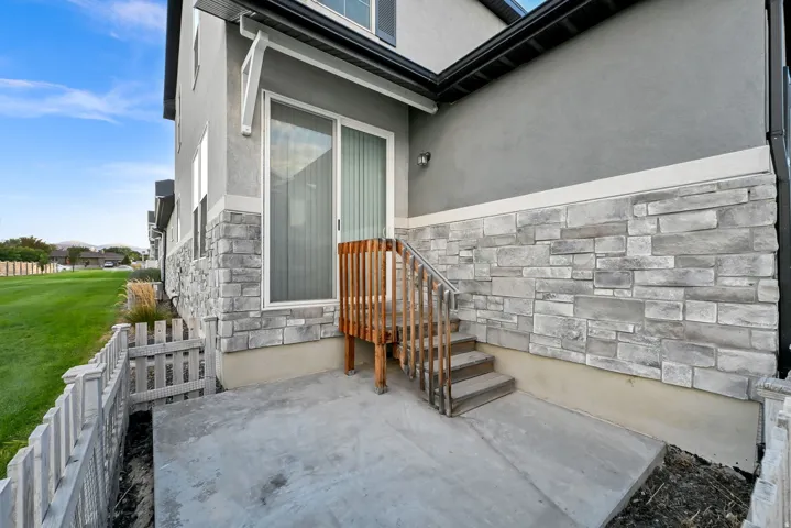 Concrete patio featuring wood stairs and railing, stone veneer siding, and a sliding glass door