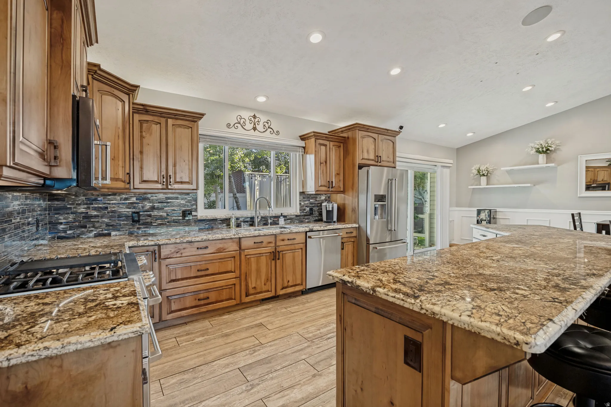 Kitchen featuring wood-finish cabinetry, granite countertops, stone tile backsplash, stainless steel appliances, and recessed lighting