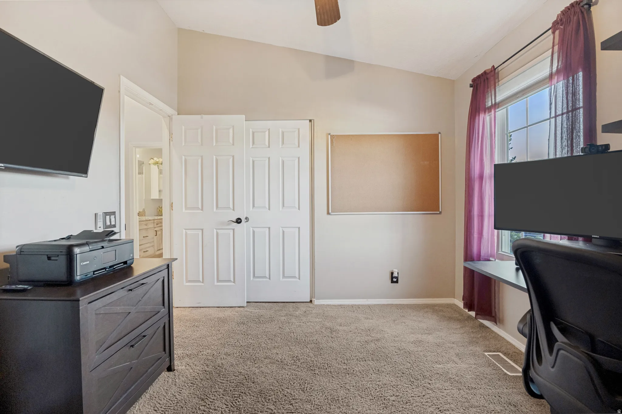 Vaulted ceiling with a ceiling fan, carpet flooring, and a window with a built-in desk