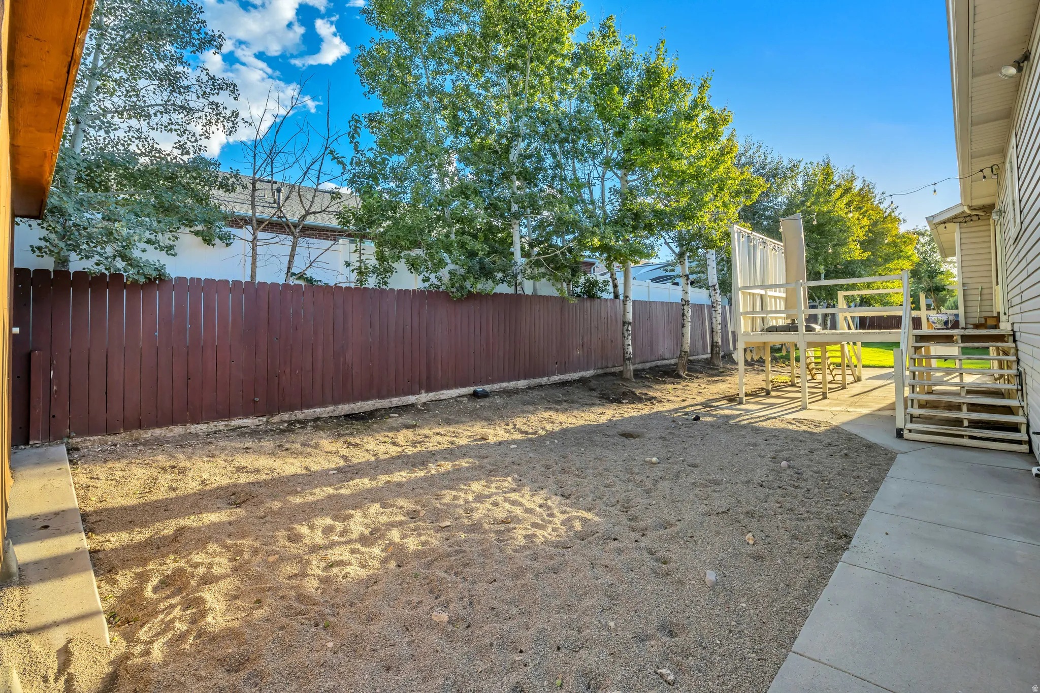 Spacious backyard with a wood privacy fence, concrete patio, multi-level deck structure, and mature trees
