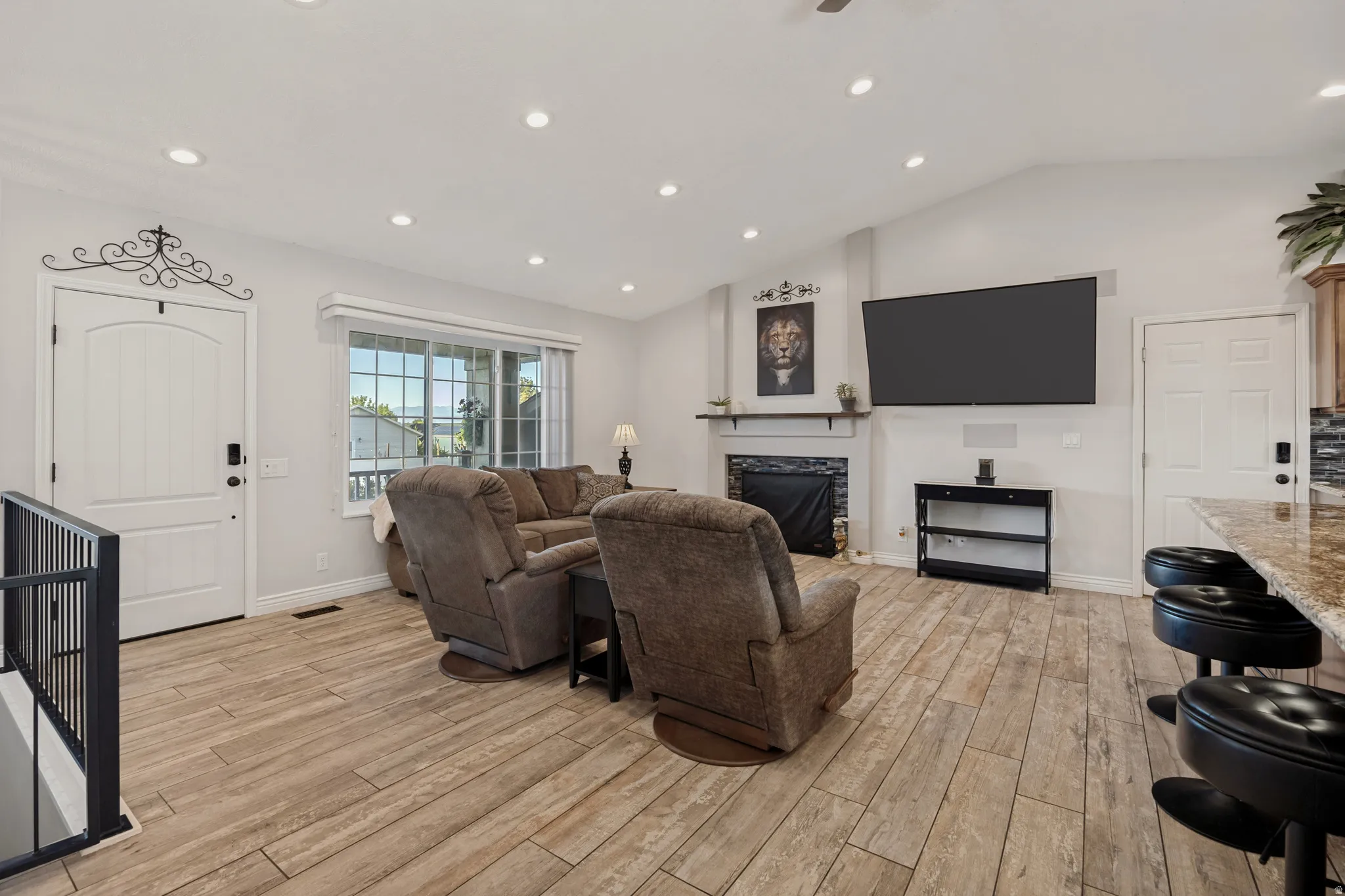 Living area featuring wood-finish flooring, a fireplace with a stone surround, a vaulted ceiling with recessed lighting, and a window with a built-in blind