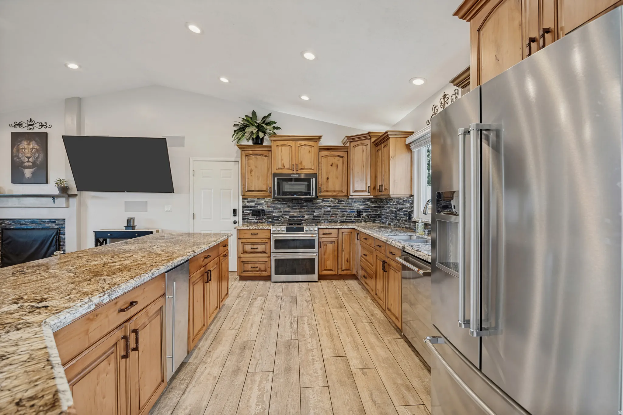 Spacious kitchen featuring an expansive island with stone countertops, wood-finish flooring, stainless steel appliances, and wood cabinetry