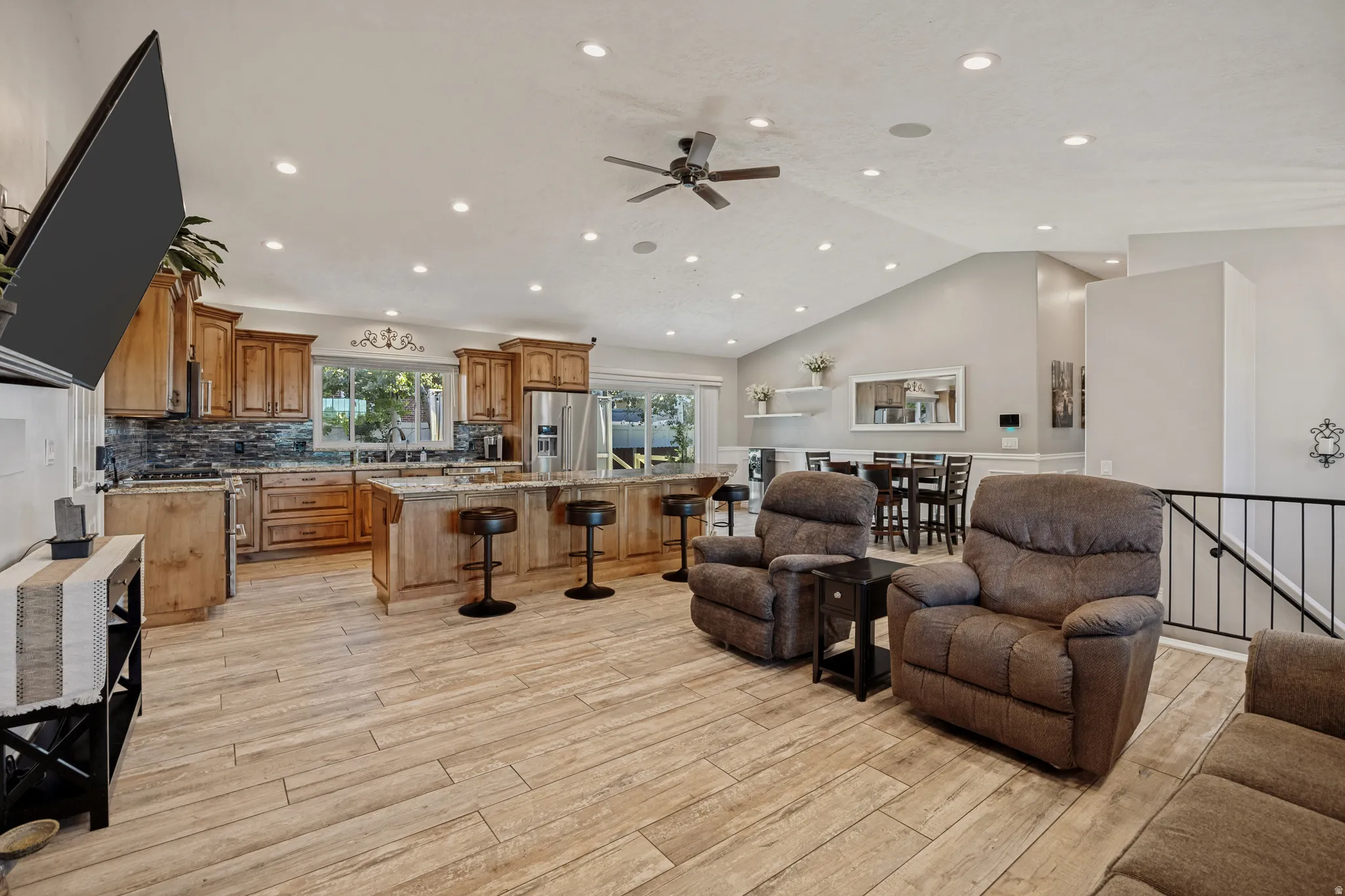 Open-concept living area with wood-finish flooring, vaulted ceilings, recessed lighting, and a ceiling fan